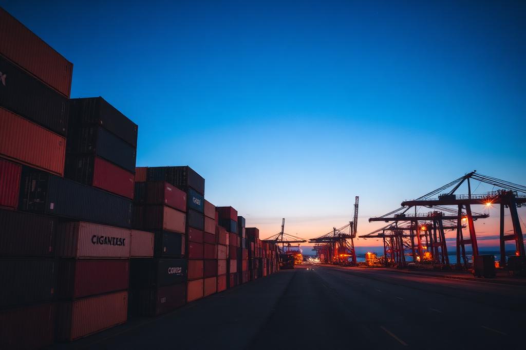 Stacked shipping containers at a working port at dusk